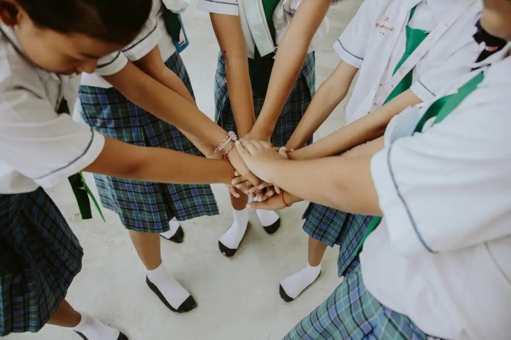 Group of students in school uniforms joining hands symbolizing unity and teamwork.