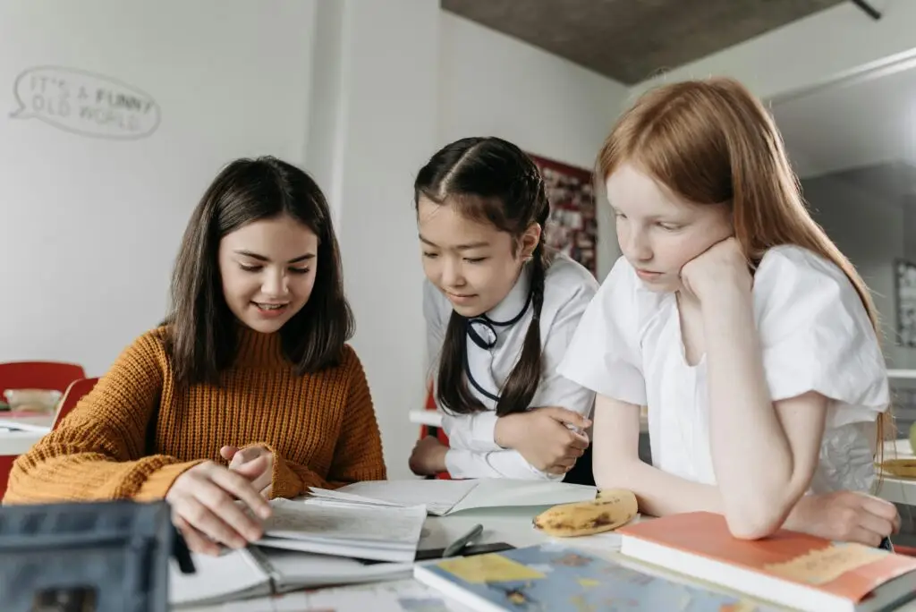Three diverse schoolgirls working together over books in a classroom setting, fostering education and collaboration.