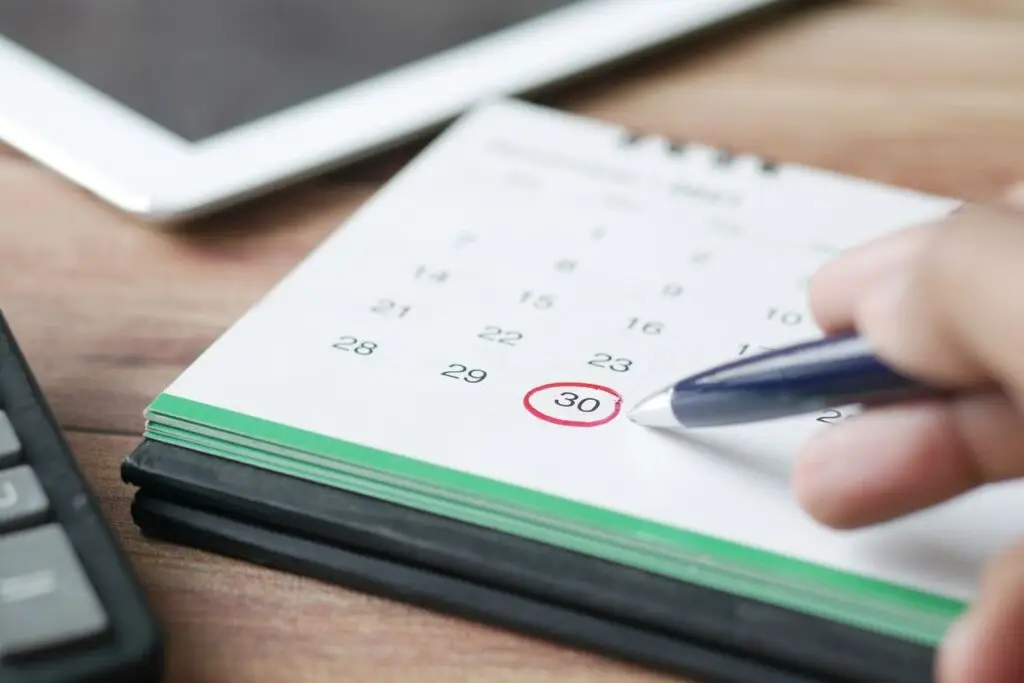 Close-up shot of a hand marking a date on a calendar with a pen, emphasizing planning and scheduling.