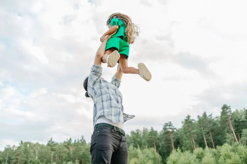 Joyful moment of a father playfully lifting his daughter in the air outdoors.