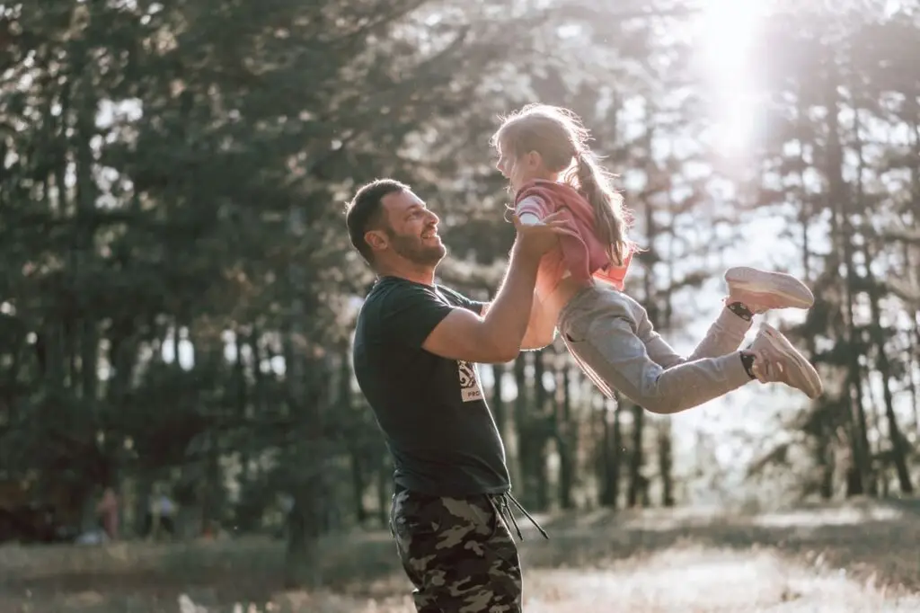 A joyful moment between a father and daughter playing in a sunny forest, capturing love and happiness.