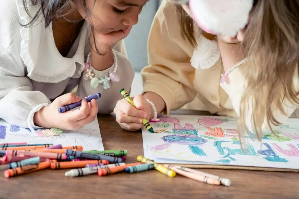 Crop multiethnic little girls leaning on hands and drawing greeting poster while preparing for Easter celebration together