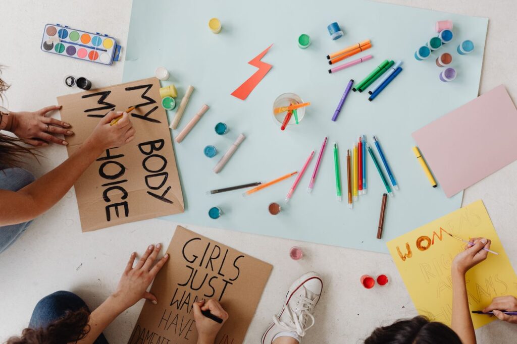 Hands crafting protest signs with slogans like 'My Body, My Choice' using markers and paints.