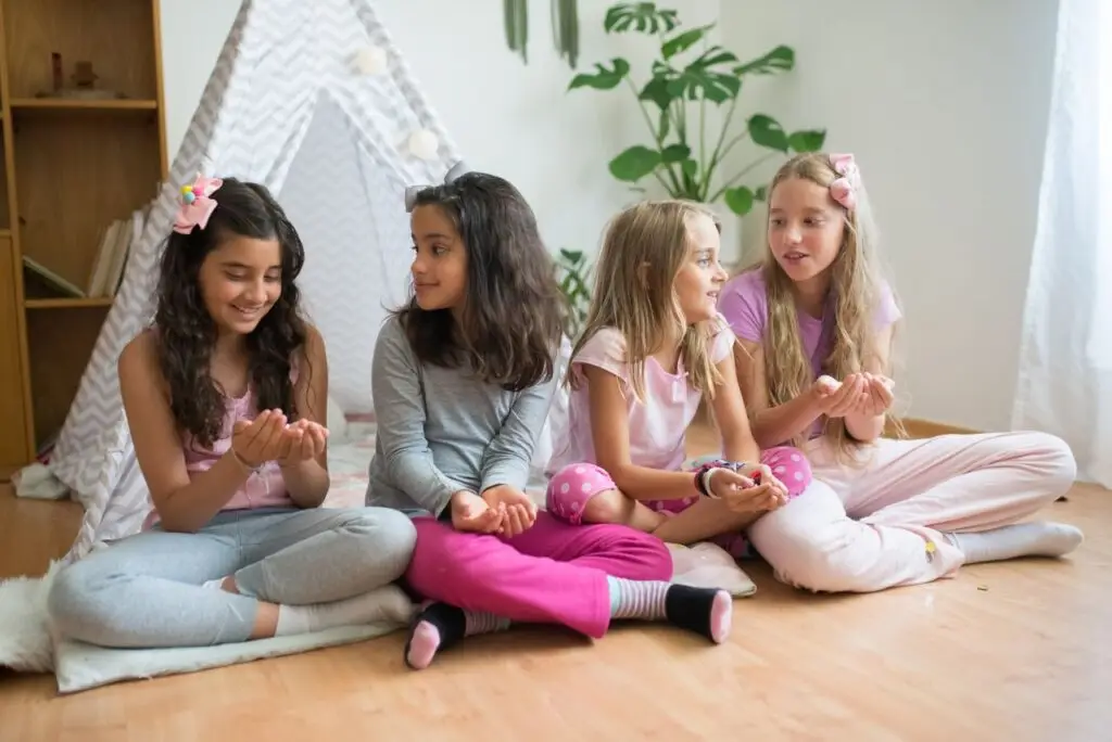 Four girls enjoying a cozy pajama party indoors, seated in a tent, sharing laughter and friendship.